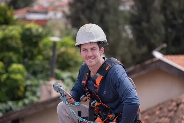 עובד עם רתמת בטיחות מנקה פאנלים סולאריים על גג בית מגורים