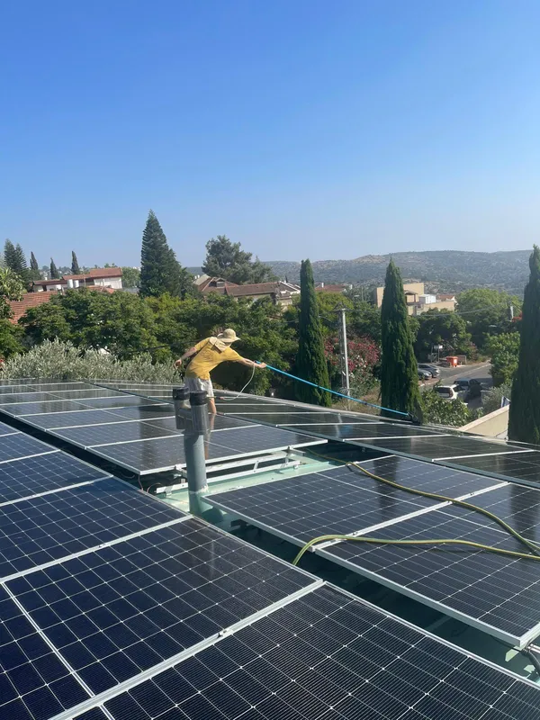 עובד מנקה מערכת סולארית על גג בשכונת מגורים