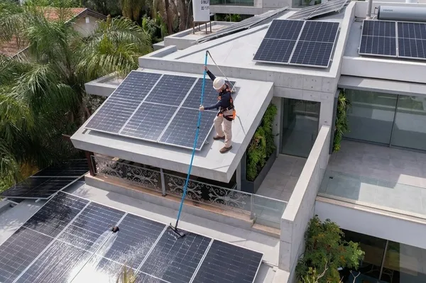 עובד מנקה פאנלים סולאריים על מרפסת בניין מודרני